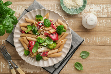 Wholegrain pasta penne with broccoli and red grilled bell pepper and on light wooden rustic background table. Vegan pasta. Traditional Italian cuisine. Flat lay. Copy space.