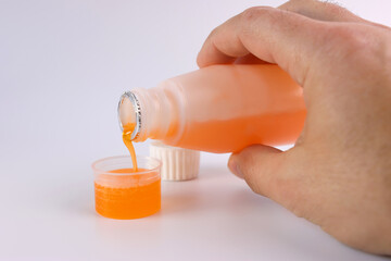 Medicinal syrup is poured into a vessel with liquid volume divisions on a white background....
