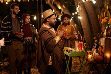 Man in traditional clothes praying at altar outdoors and celebrating the mexican holiday with other people in background