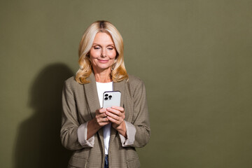 Photo of senior businesswoman influencer surf social networks using smartphone wear formal jacket isolated on khaki color background