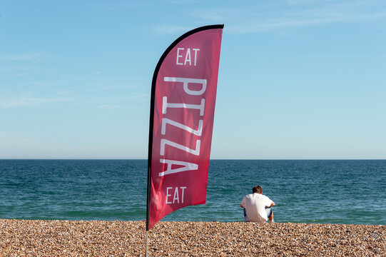 Eat pizza flag on a beach with the rear view of a man sitting with his takeaway pizza