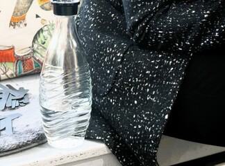 Trinkflasche mit Wasser gefüllt auf grauem Holzpodest vor sitzender Frau mit grauer Winterjacke...