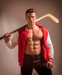 A muscular young man holding a hockey stick and wearing a red jacket open on muscle torso. A Strong Man Ready to playing hockey