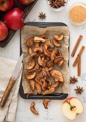 Brown dried apple slices on baking tray with cinnamon and red ripe apples.Macro.