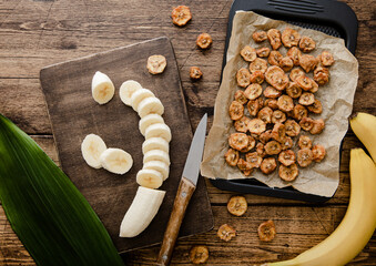 Fresh raw banana slices with dried banana chips on wooden background with green leaf.Top view - obrazy, fototapety, plakaty