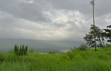 Panoramic view of lush green landscape and Sahyadri mountains with clouds in Tapola, a famous tourist place during monsoons in Maharashtra, India