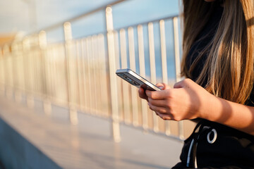 A teenage girl holds a smartphone in her hands and chats on the city embankment in summer