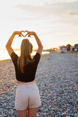 A teenage girl on the seashore on the beach at sunset made a heart out of her fingers