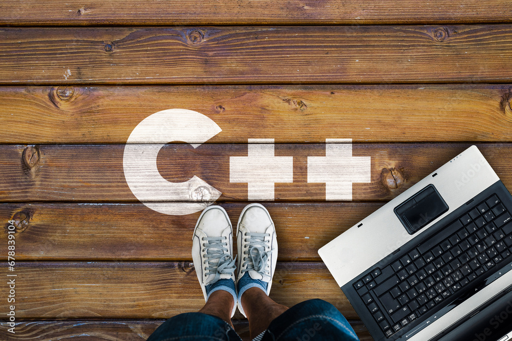 Poster Legs in sneakers standing next to laptop and c++  on wooden floor. C++  programming language. 
