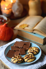 Cup of tea or coffee, plate with desserts, dried oranges, bowl of grapes, scented candles, vintage books, pumpkins and autumn leaves on the table. Autumnal hygge. Selective focus.