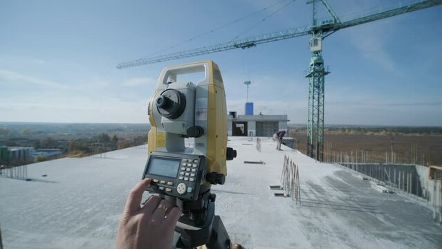 Geodetic works. Surveyor engineer in protective wear and red helmet using geodetic equipment at construction site. Professional equipment.
