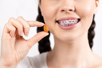 Close up of young Caucasian smiling woman with brackets show almond nut. White background. Concept...