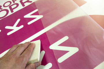 A worker's hand with a soft felt squeegee for vinyl film stickers. Decoration of shop windows with inscriptions. Advertising for the store.