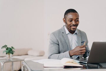 African american businessman reading email with good news at laptop at office desk, smiling
