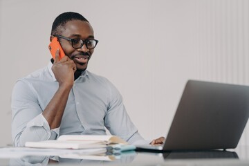 Fototapeta premium African american businessman talk on phone at laptop, consulting client, discussing business project
