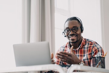 African american man wearing headset communicates with client by video call at laptop. Remote work