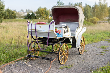 A beautiful empty carriage stands without a horse on a rural road. The elegant white carriage...
