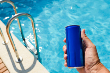 A can of drink in hand against the backdrop of a hotel pool. Close-up, blue aluminum can