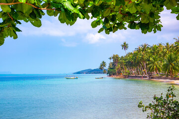 Tropical seascape. Sandy beach with palm trees and fishing boats in the sea in Thailand.