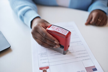 Hand of young African American female worker of visa application center stamping document while...