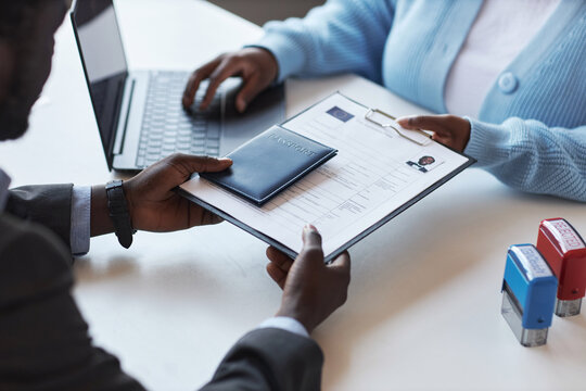 Hands of young African American male applicant passing documents and passport to female manager of visa application center