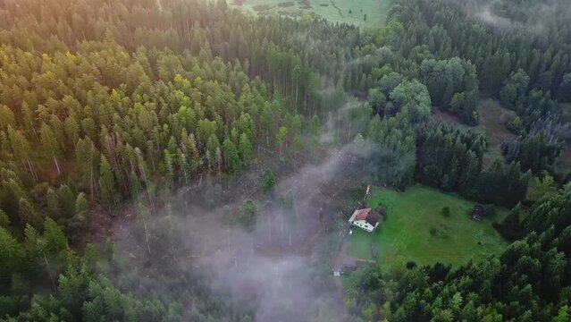 Drone shot of lonely house in middle of Bavarian Forest, surrounded by clouds