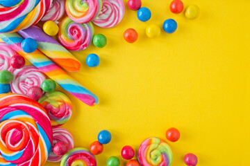 Various lollipops and round candy in bright and bold colours on a yellow background, with space for...