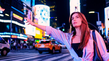 Background of night city in neon lights. Young attractive woman is gesturing for call taxi driver. Beautiful charming girl walking on night street. Social meeting date with friends at night.