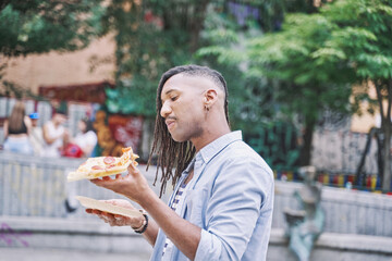 portrait of a latin man walking through the city eating a slice of pizza. fast food