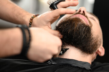 Obraz na płótnie Canvas A barber in the salon trims the beard of a man with a trimmer in the neck area