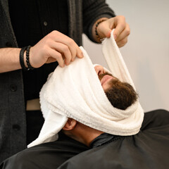 The barber covers the client face with a hot wet towel to steam off the beard.
