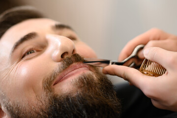 A barber stylist trims a Caucasian mans mustache with scissors - obrazy, fototapety, plakaty