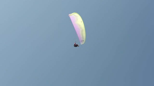 Close up from below of a colorful paraglider spiraling against a background of blue summer sky