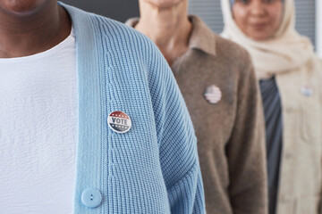 Close-up of young African American woman in blue cardigan with vote badge on chest standing in...