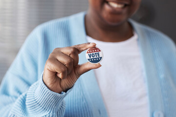 Focus on hand of young African American woman in casualwear holding small round vote badge while standing in front of camera - obrazy, fototapety, plakaty