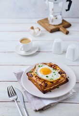 Hot croque madame sandwich with ham, cheese and fried egg on a white plate on a light wooden background. Sandwich recipes, hot breakfasts.