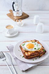 Hot croque madame sandwich with ham, cheese and fried egg on a white plate on a light wooden background. Sandwich recipes, hot breakfasts.