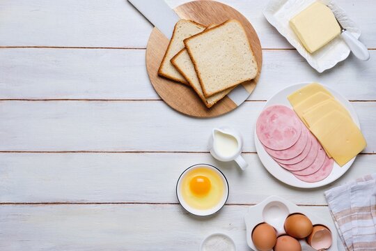 Prepared ingredients for making a hot croque madame sandwich on a white wooden background. Recipes for sandwiches, hot breakfasts.