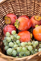 ripe Kaki Persimmon fruit and grapes in wicker basket