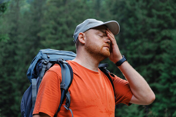 Bearded male hiker covering face with hand during trip