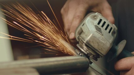 Close-up shot of hands of unrecognizable industrial worker using angle grinder on pipe, sparks flying during metal cutting process