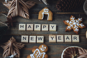 Happy New Year greeting written with wooden blocks . Holidays card on wooden background with gingerbread cookies, handmade craft toys, festive rustic zero waste decorations. Sustainable lifestyle