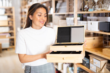 Portrait of young woman choosing wooden jewelry organizer at store of household goods
