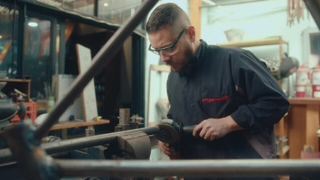 Professional metalworker in safety glasses performing metal cutting with an angle grinder, sparks flying to the sides in workshop