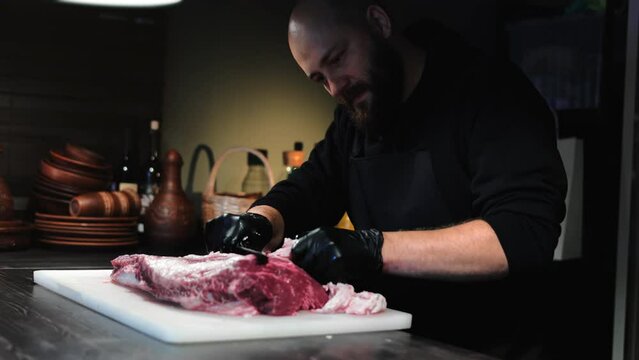 Brutal male chef cooking meat steak cutting fat from fillet use knife on marble board at kitchen