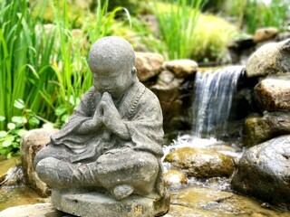 Fototapeta na wymiar Close-up of a buddha meditation statue with a cascade in the blurred background