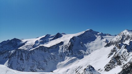 Fototapeta na wymiar Aerial view of snowy rocky mountains on blue sky background