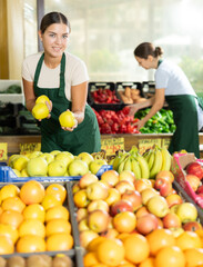 Smiling girl seller is showing assortment of fresh apples in vegetable shop
