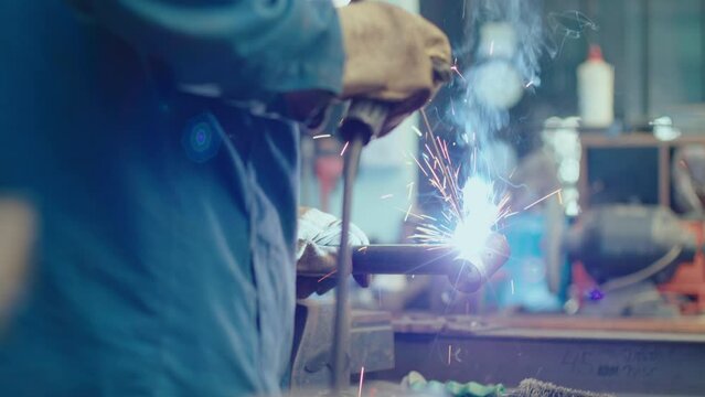 Metalworker in protective helmet and gloves welding pipe with welding torch making flame and sparks in the repair workshop