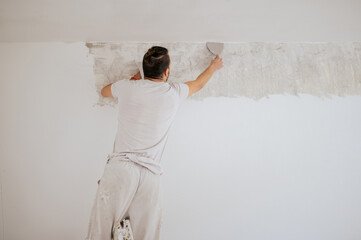 Builder on ladder using spatula for plasterwork and skim coating walls.